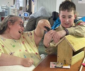 A boy scout and resident Kim are sitting at a table building a birdhouse.