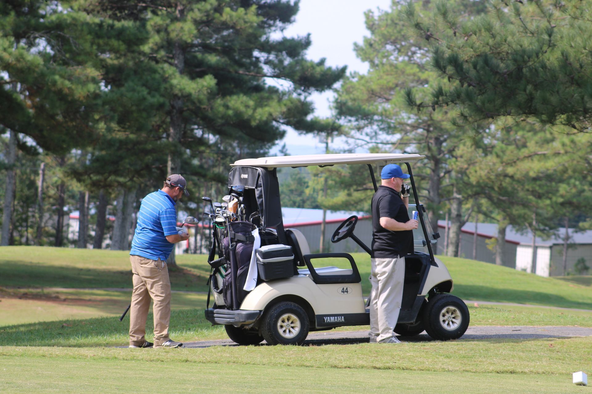 Two men are standing next to a golf cart on a golf course at a safehaven golf tournament.