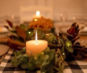 A lit candle is sitting on a table with a wreath of leaves.