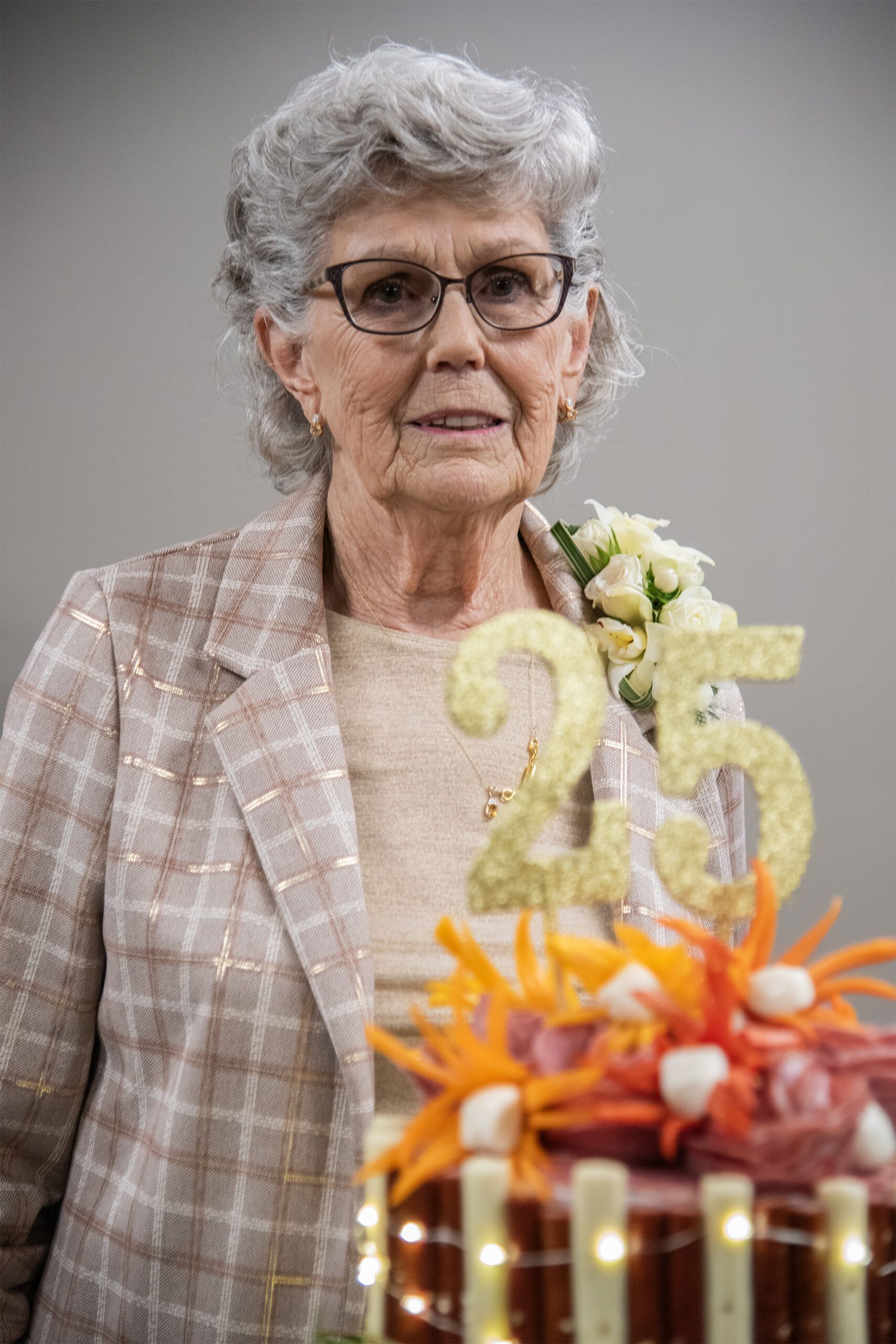 A  woman is standing in front of a cake to celebrate 25 years.