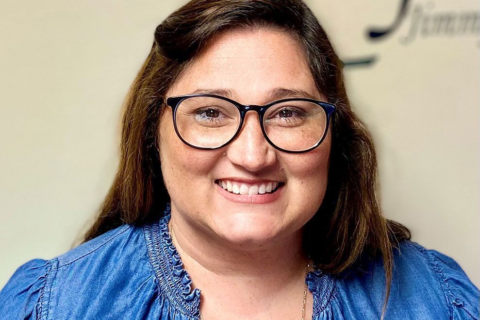 A woman wearing glasses and a blue shirt is smiling for the camera.
