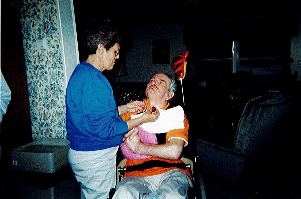 A woman providing caring to a man in a wheelchair with a traumatic brain injury.
