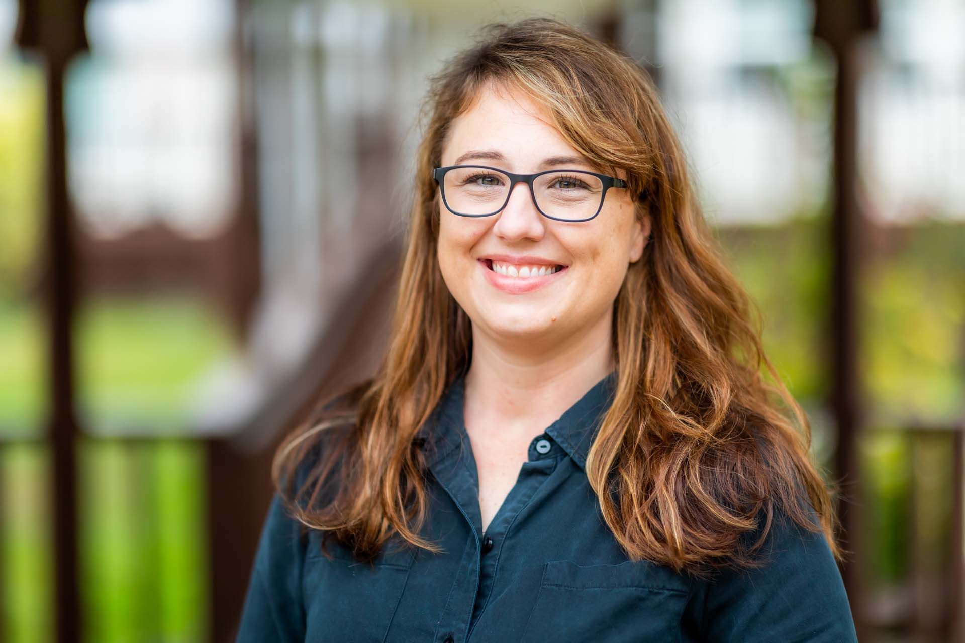 A woman wearing glasses and a blue shirt is smiling for the camera.