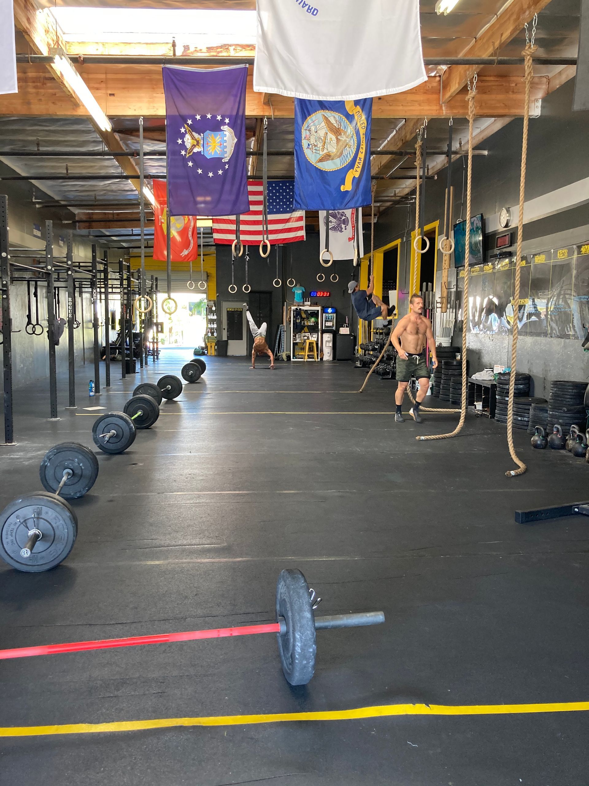 CrossFit gym interior with barbells on the floor, hanging rings, and flags overhead