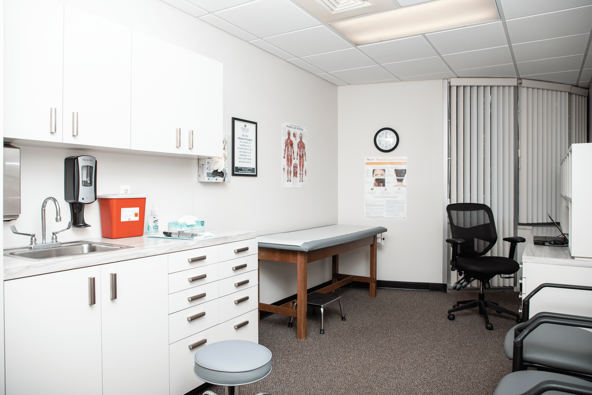 A doctor 's office with a table and chairs and a sink.