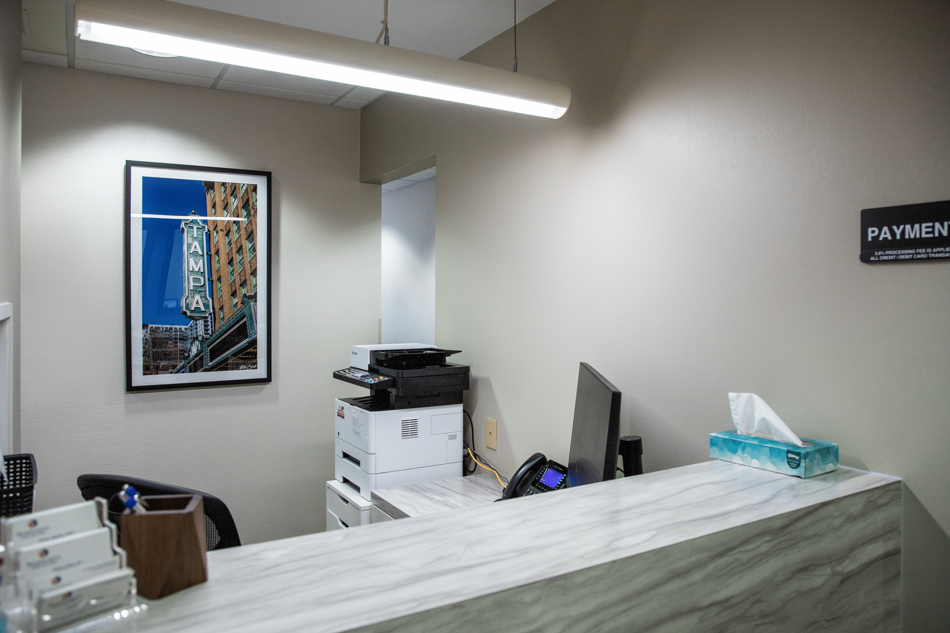 A reception desk with a computer and a picture on the wall.