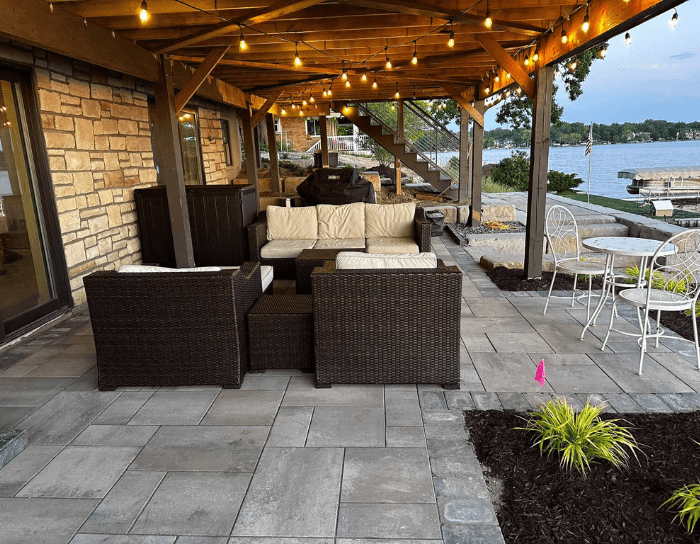 A patio with a couch and chairs under a canopy overlooking a lake