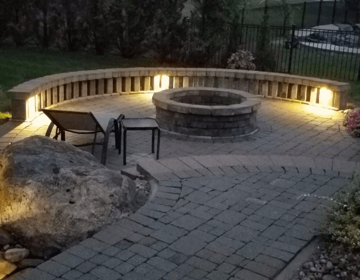 A fire pit is lit up at night on a brick patio