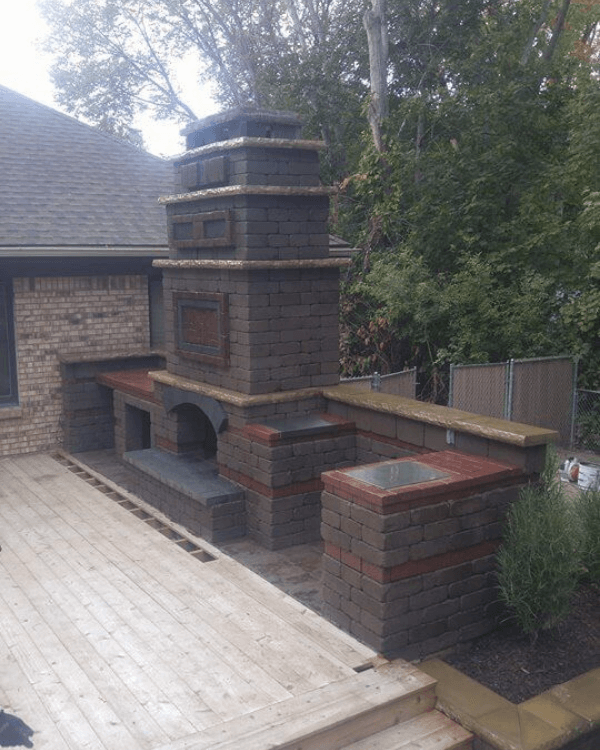 A brick fireplace sits on a wooden deck in front of a brick house