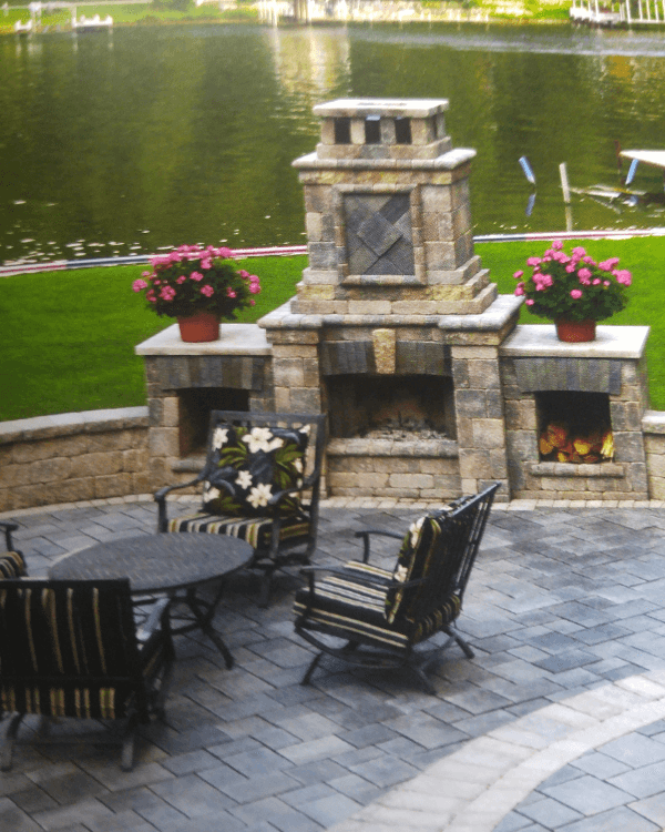 A patio with chairs a table and a fireplace overlooking a lake