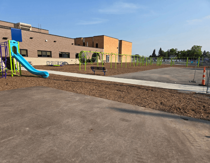 A playground with a slide and swings in front of a building
