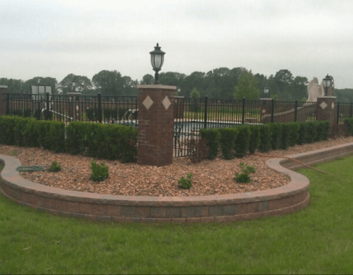 A brick wall surrounds a swimming pool with a fence around it