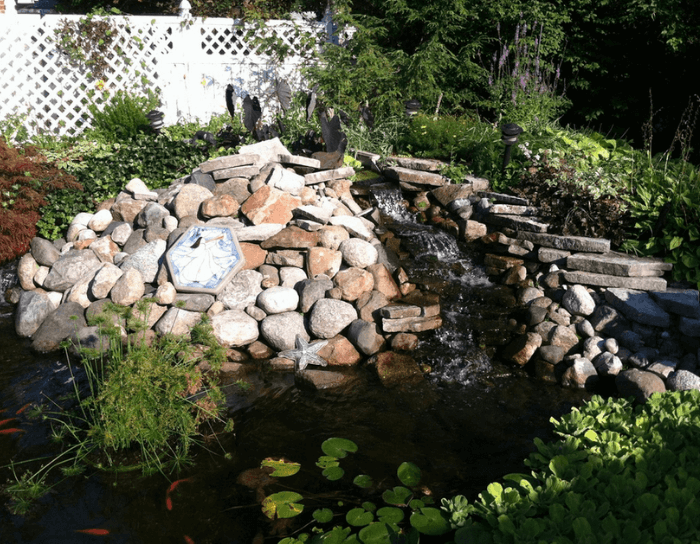 A waterfall in a garden with a white fence in the background