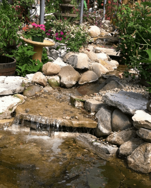 A waterfall is surrounded by rocks and flowers in a garden