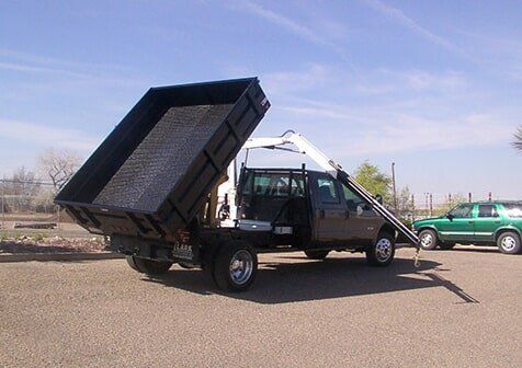 A dump truck with its bed raised, ready to unload material.  The truck is parked on gravel.