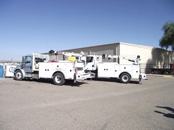 Two white utility trucks parked on asphalt, near a building.