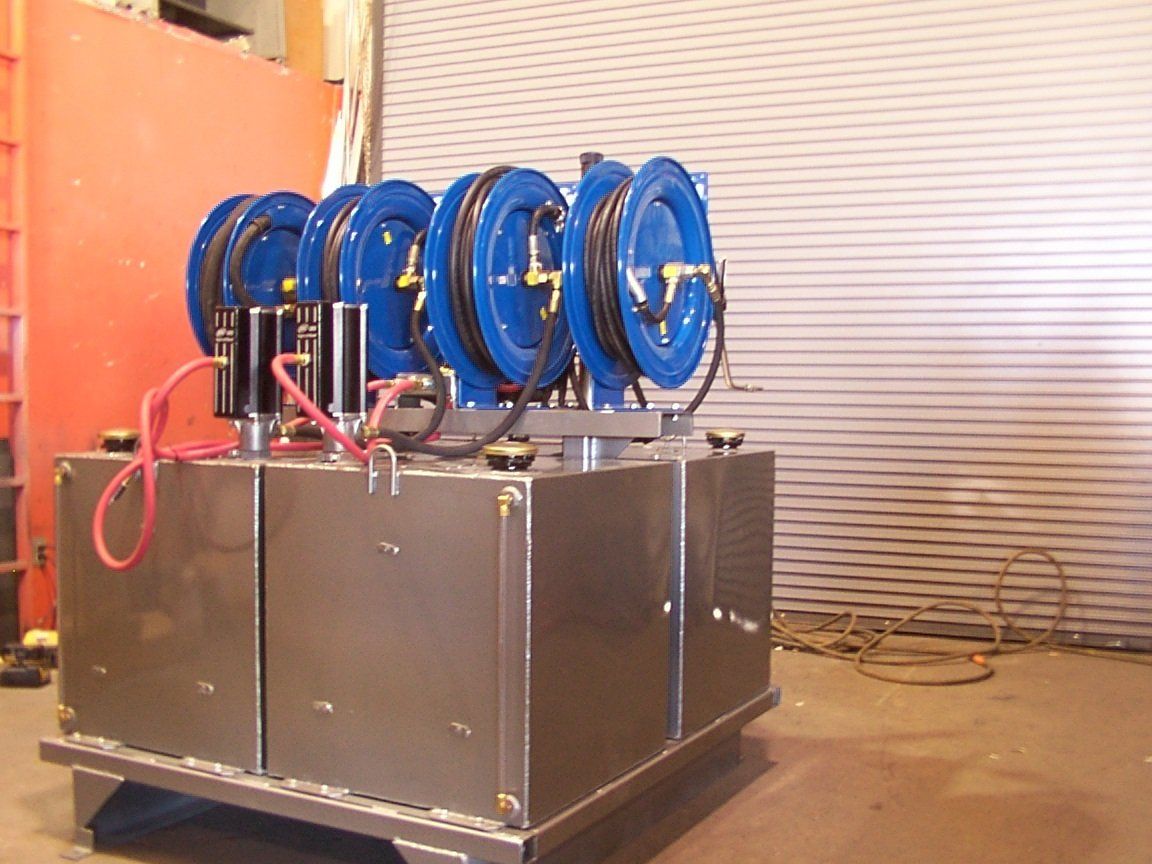 Four blue hose reels mounted on a silver box, likely a mobile system, in a workshop setting.