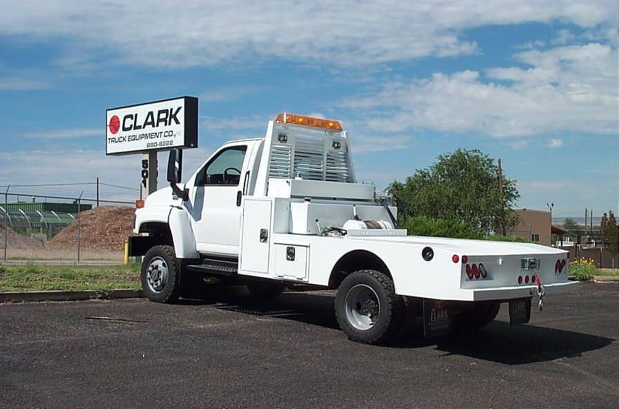 White flatbed truck parked outside a Clark Truck dealership on a sunny day.
