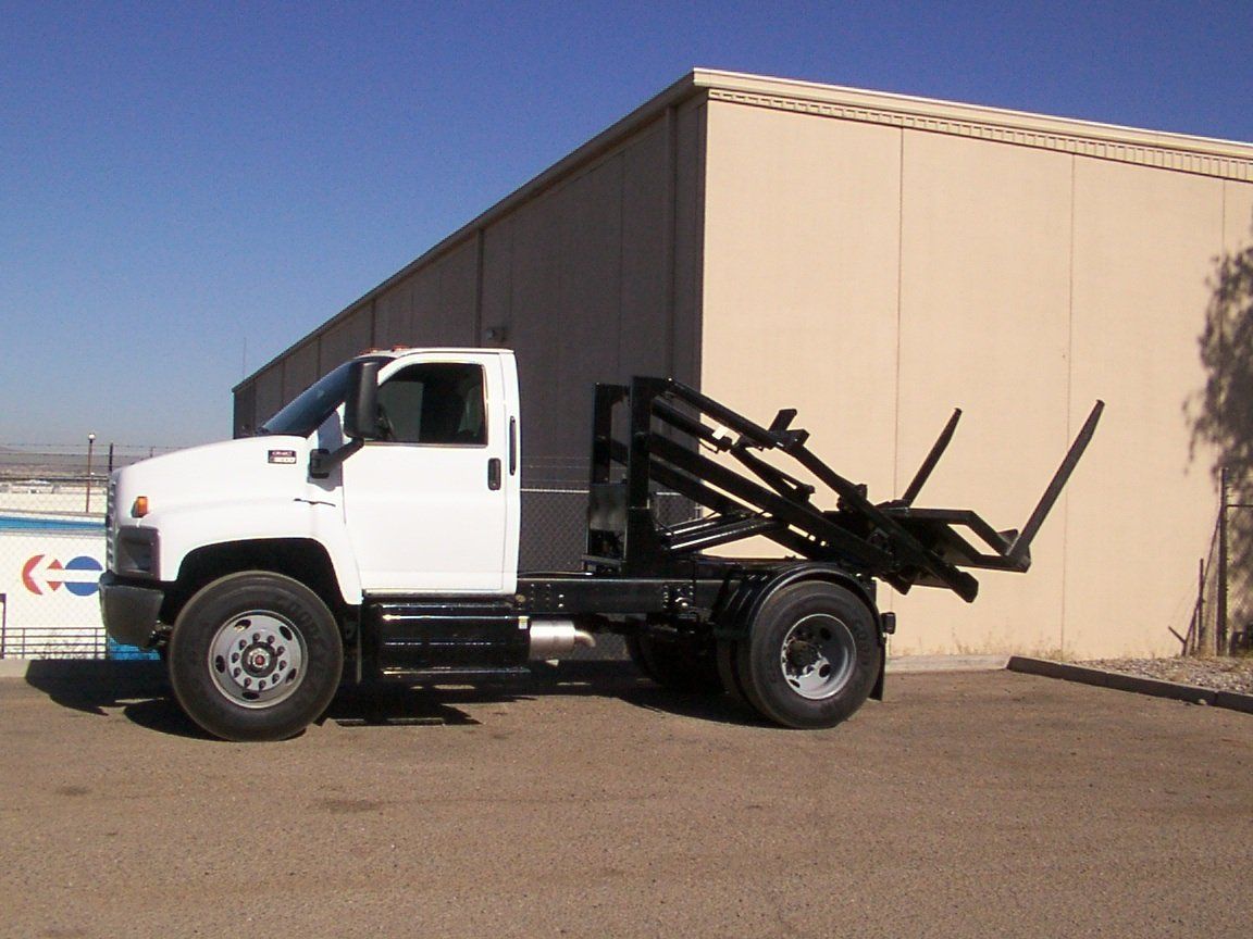 White work truck with black lift attachment parked in front of a beige building on a sunny day.