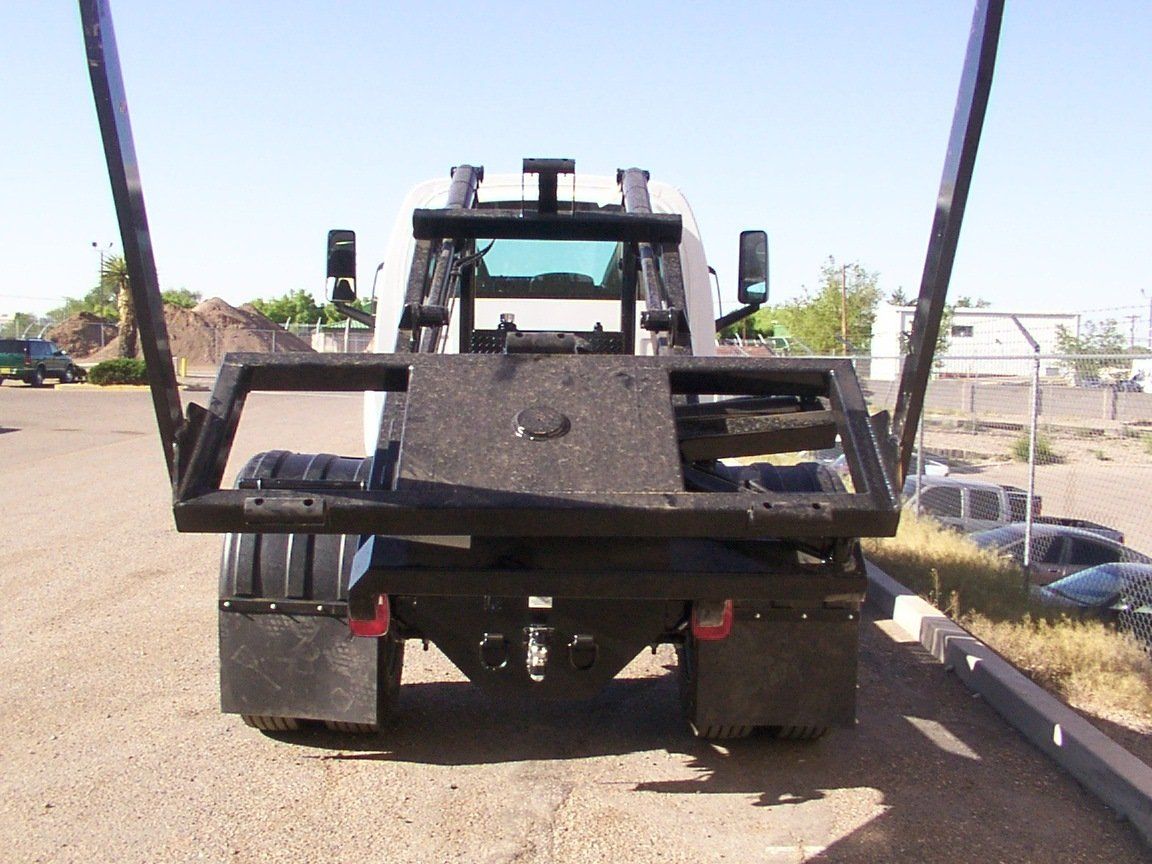 Rear view of a white truck with black platform and arms, parked outside on a sunny day.