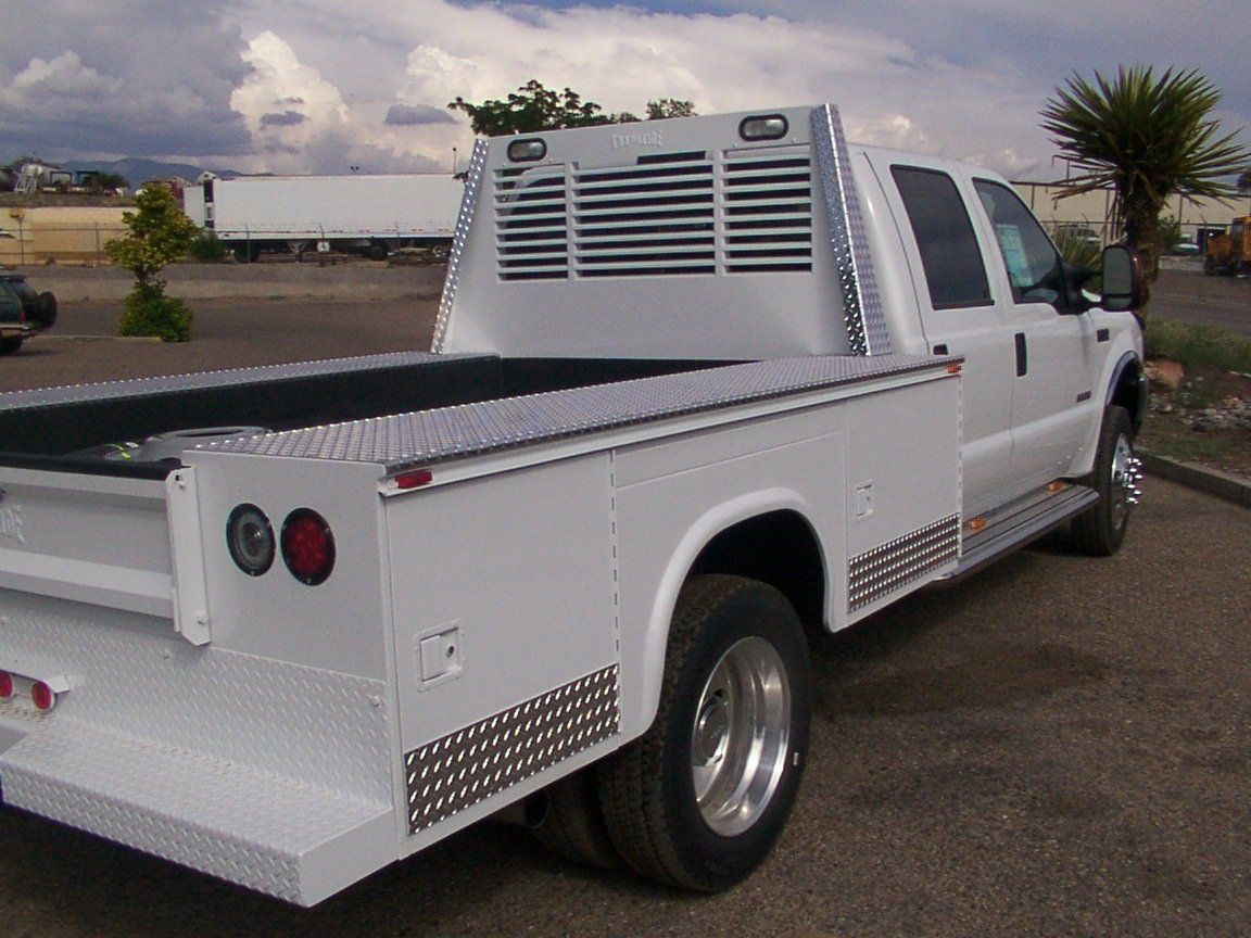 White flatbed truck with a metal frame, parked outdoors on pavement.
