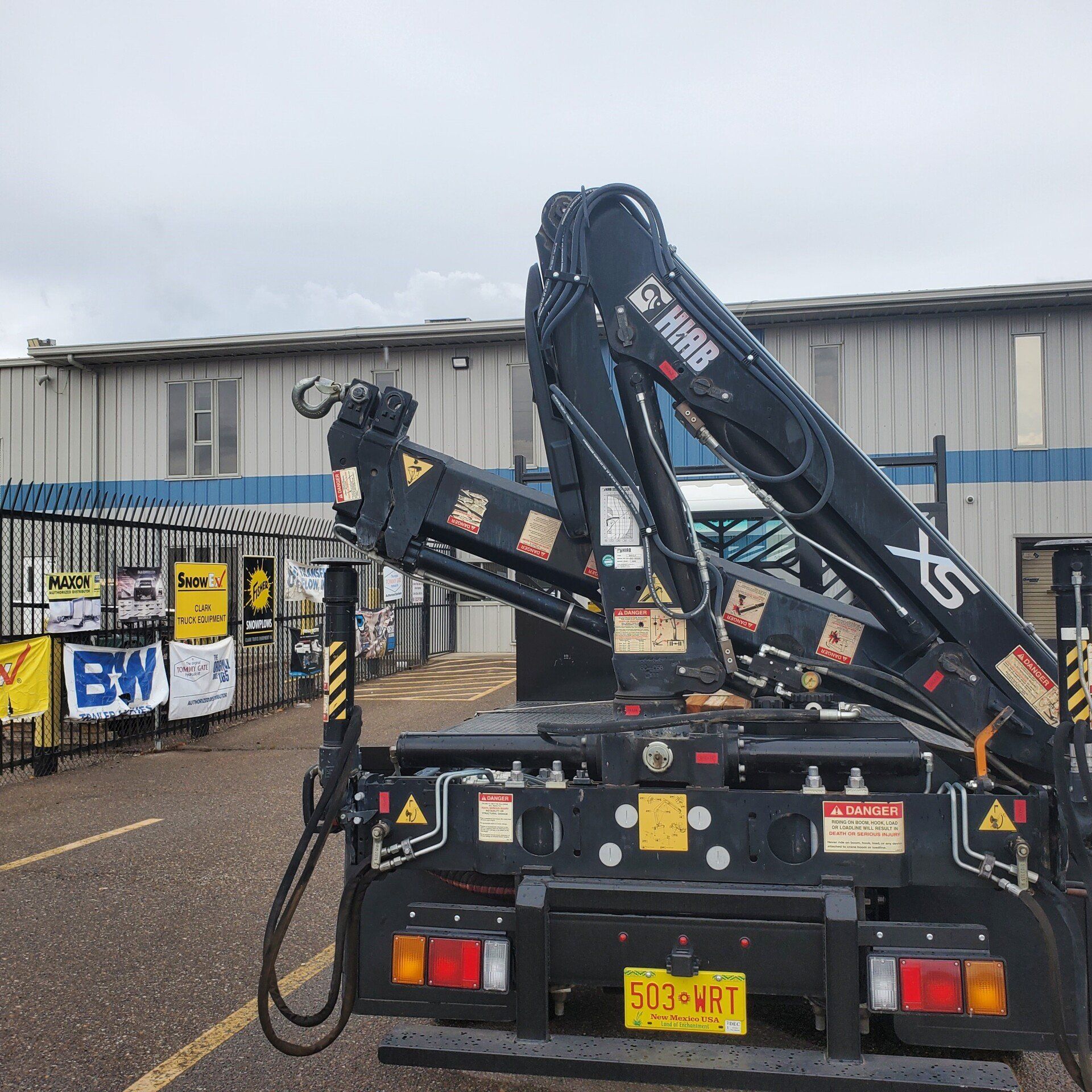 Black crane truck with its boom extended against a grey building and cloudy sky.