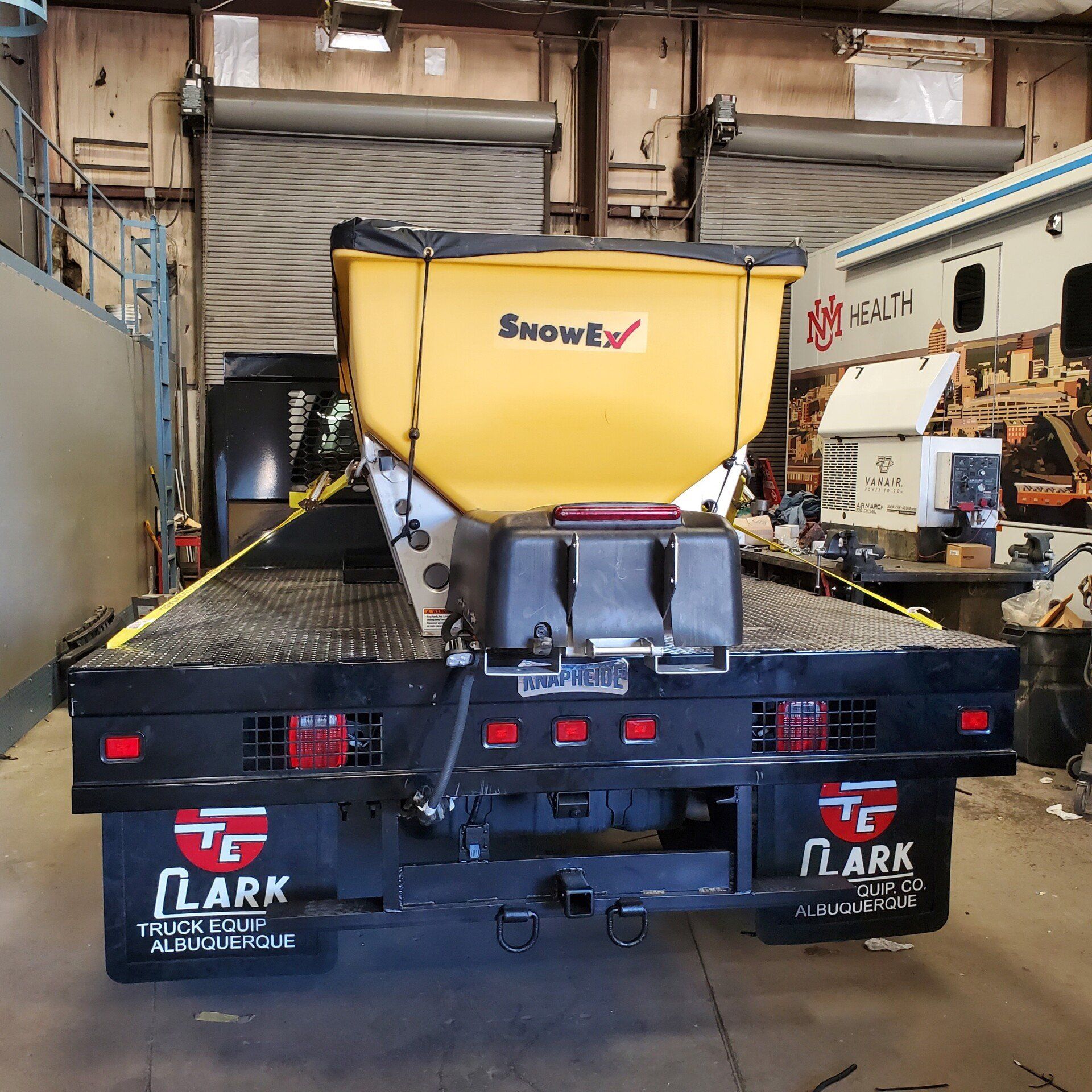 Yellow salt spreader on the back of a black truck, in a garage.
