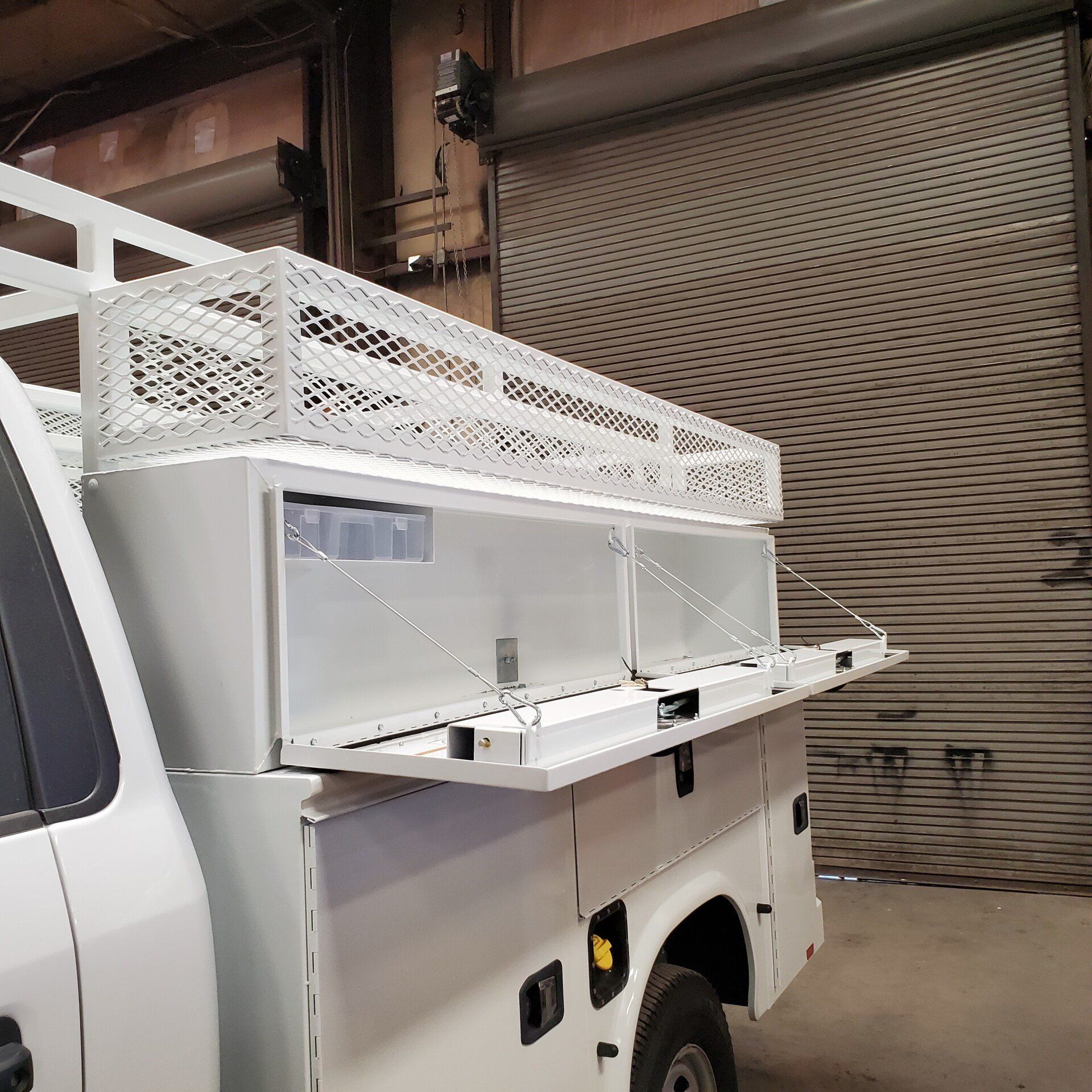 White truck bed toolbox with open compartments and wire rack.