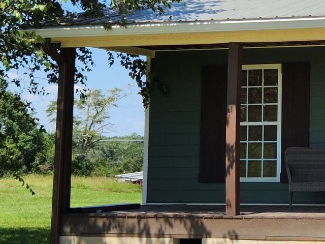 A white house with a gray roof is sitting on top of a lush green field.