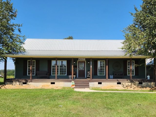 A large house with a porch and a white roof is sitting on top of a lush green field.