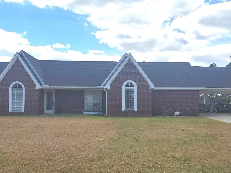 A white house with a gray roof is sitting on top of a lush green field.