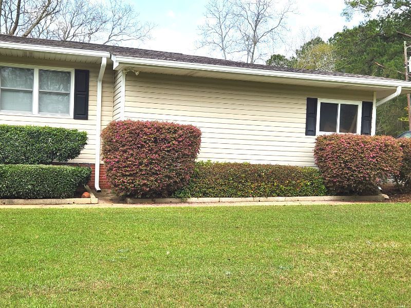 A white house with a gray roof is sitting on top of a lush green field.