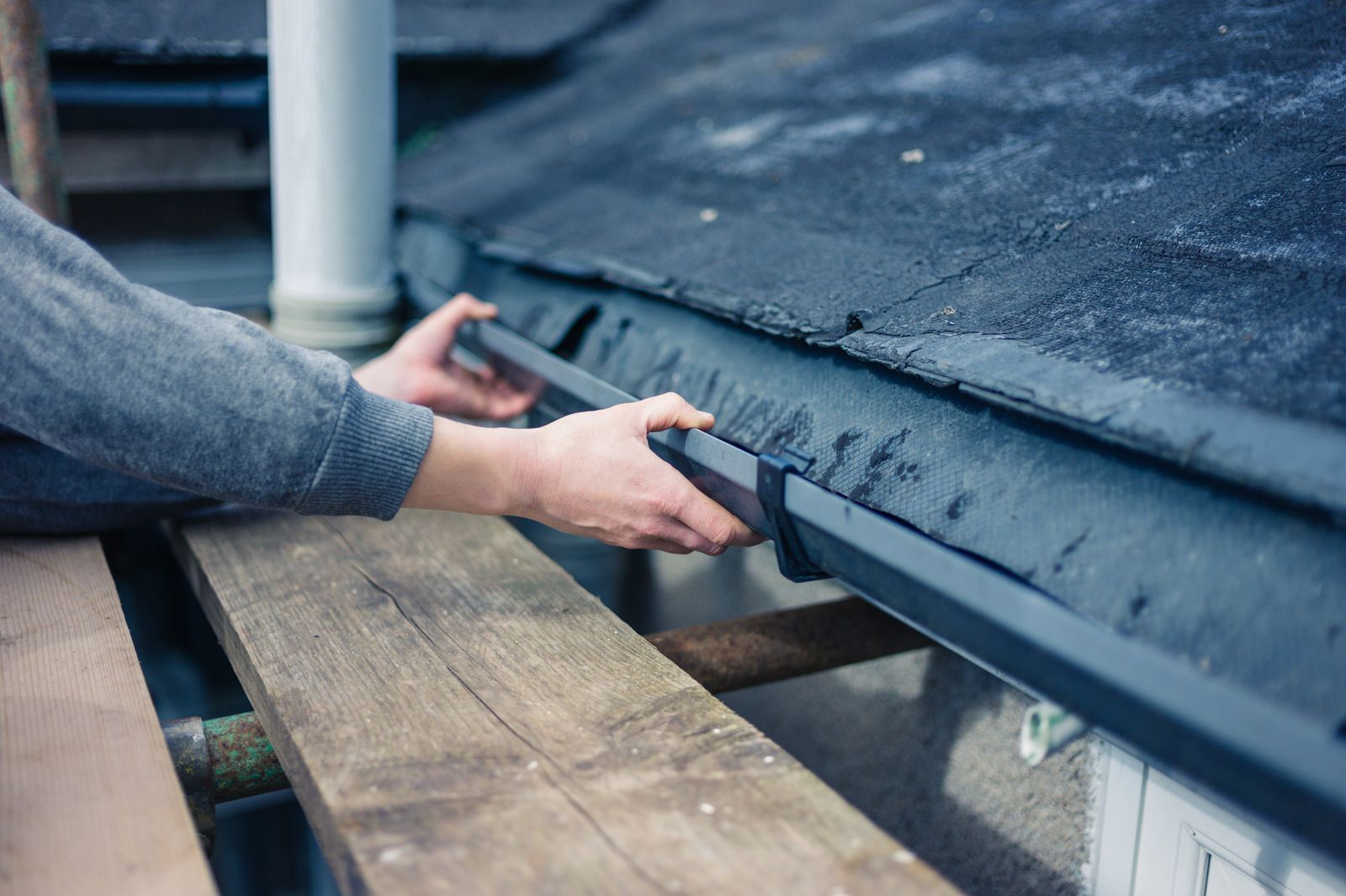 A person is fixing a gutter on a roof.