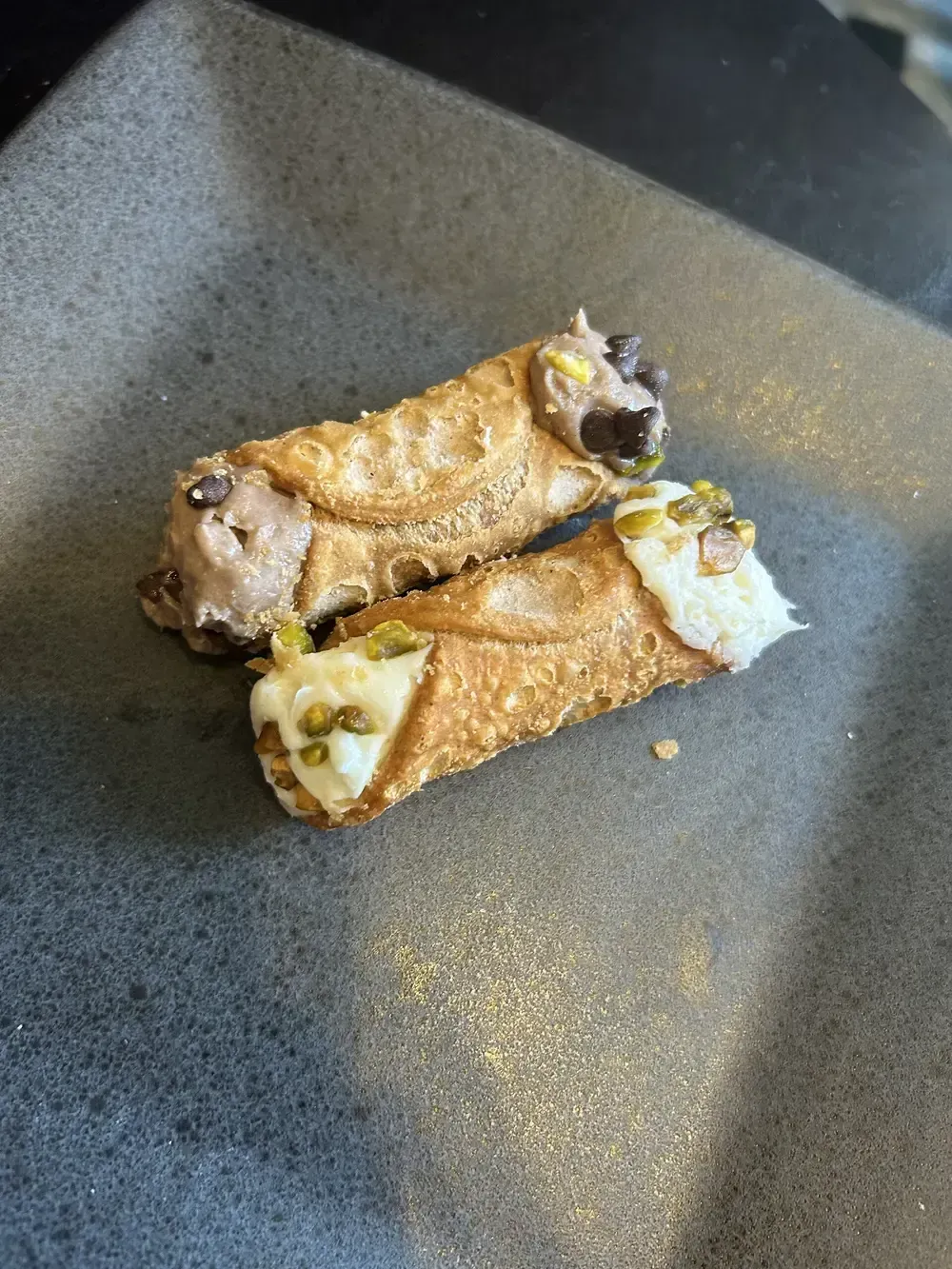Two burnt rolled crepes with filling in a black pan, dusted with sugar or spice