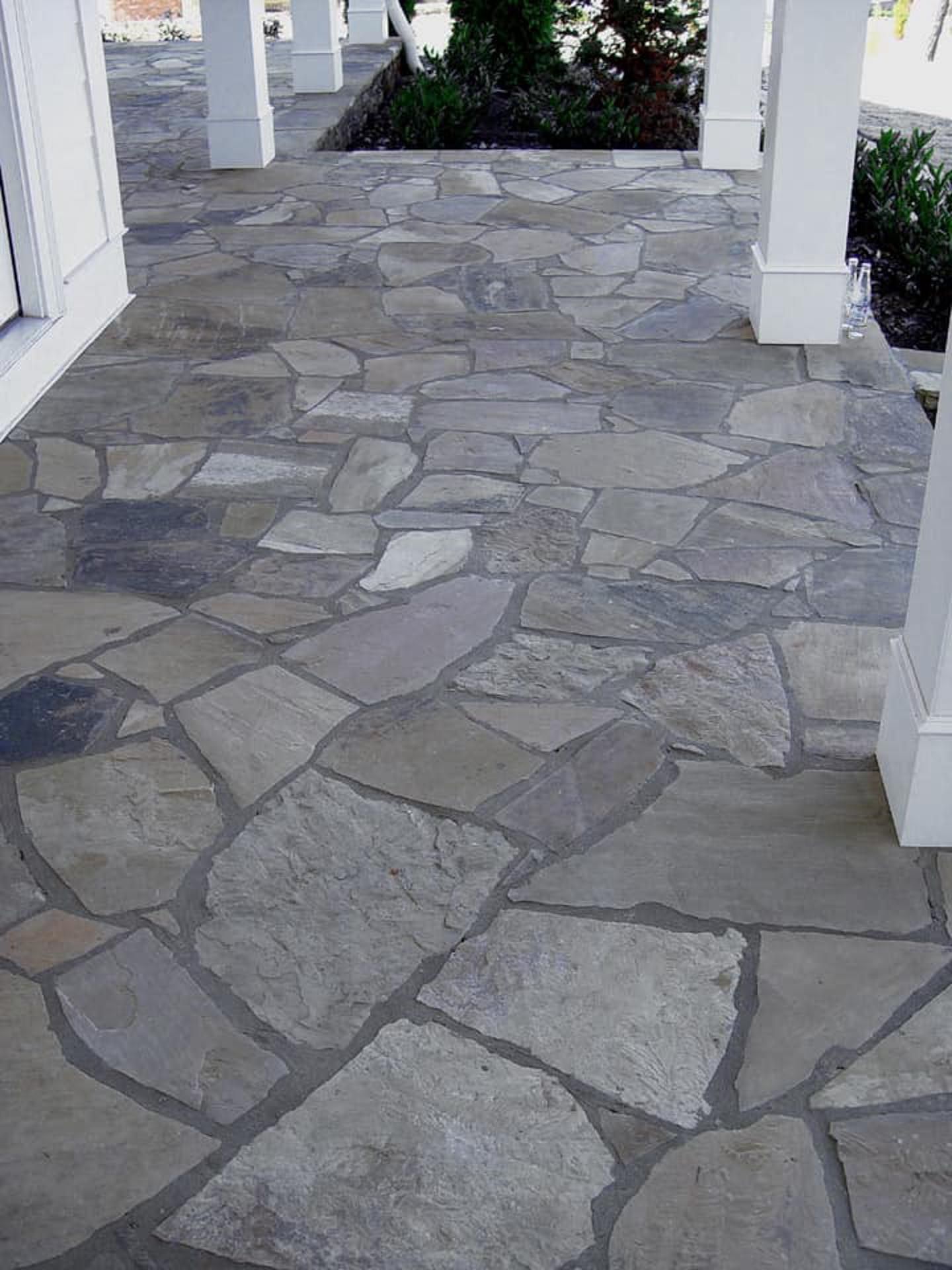A stone walkway leading to a porch with white pillars.