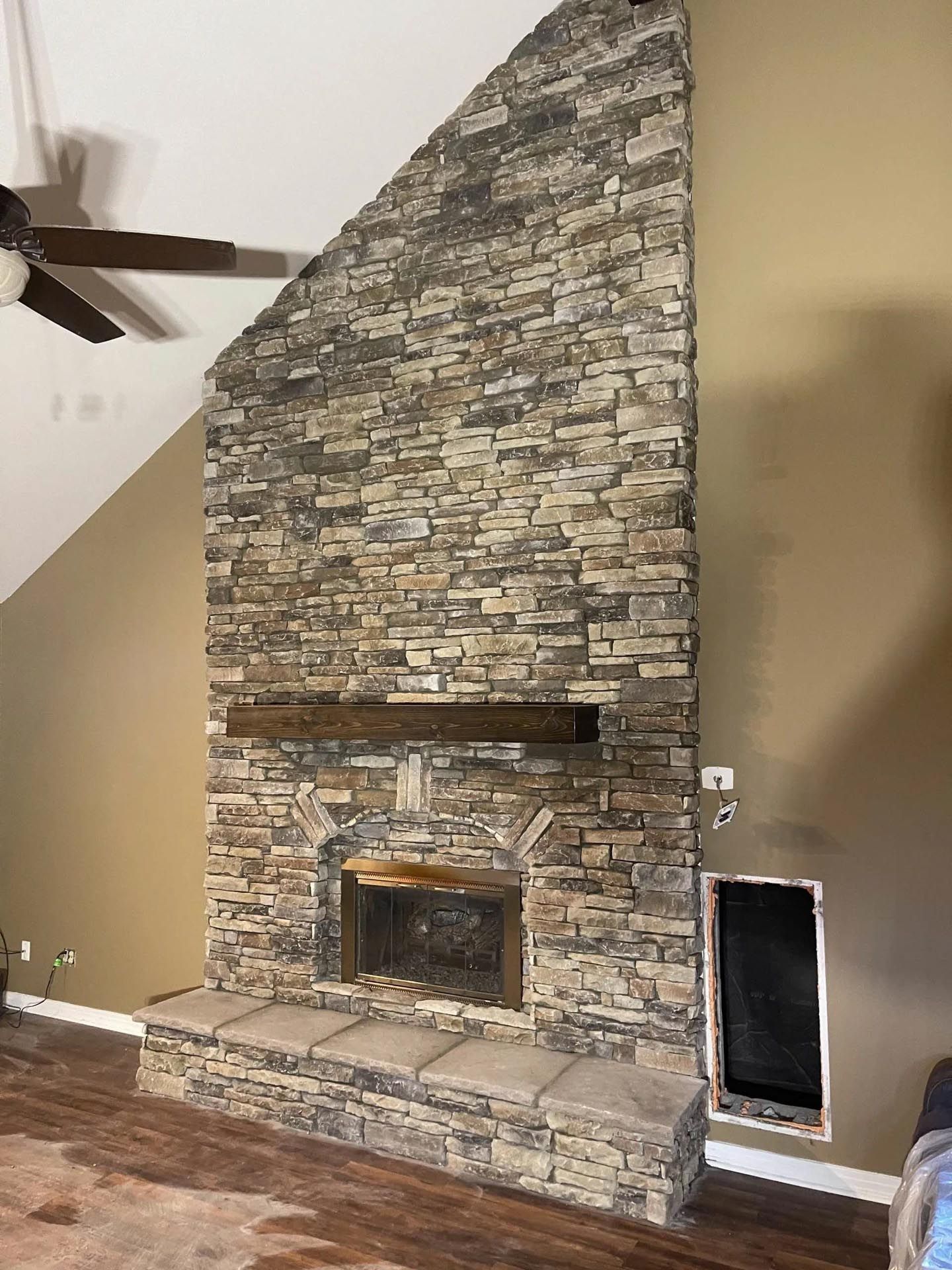 A living room with a large stone fireplace and a ceiling fan.