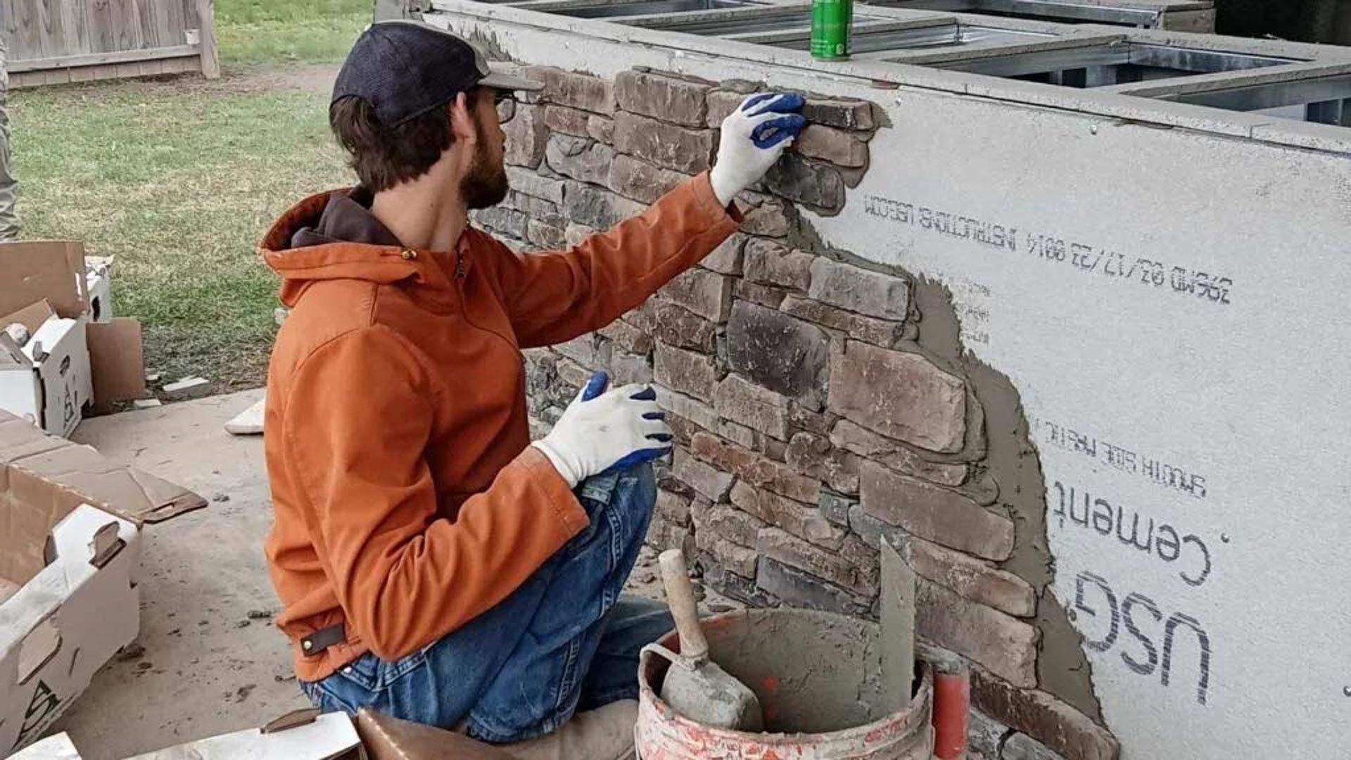 A man is kneeling down while working on a stone wall.