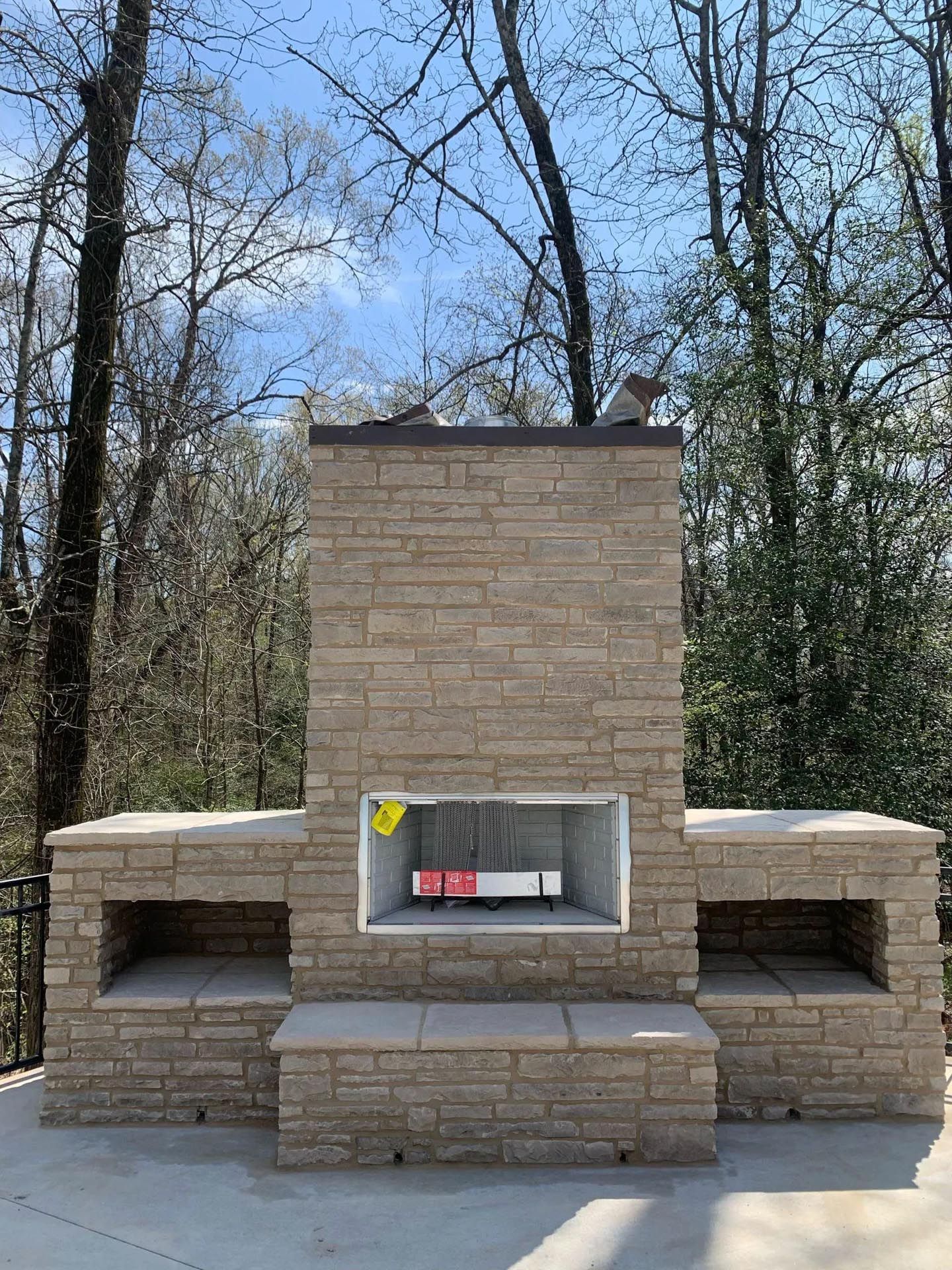 A brick fireplace on a patio with trees in the background.