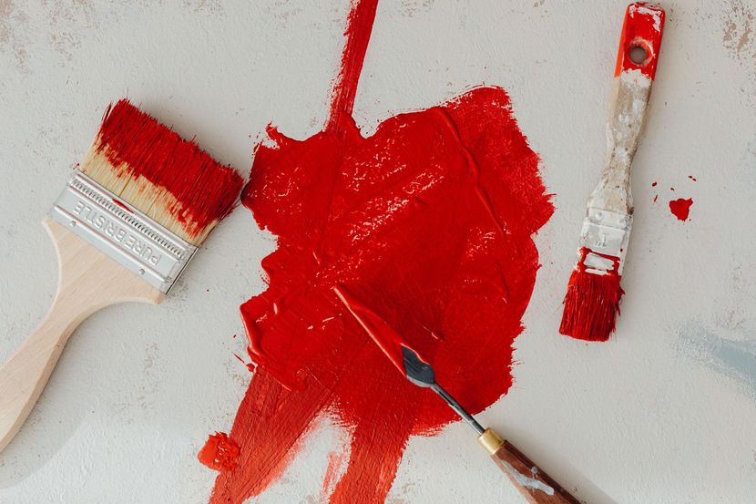 Paintbrushes and red paint splattered on a white surface
