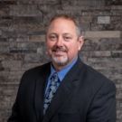 A man in a suit and tie is standing in front of a brick wall.