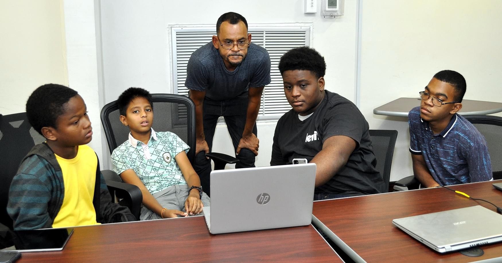 A group of young men are sitting around a table looking at a laptop computer.