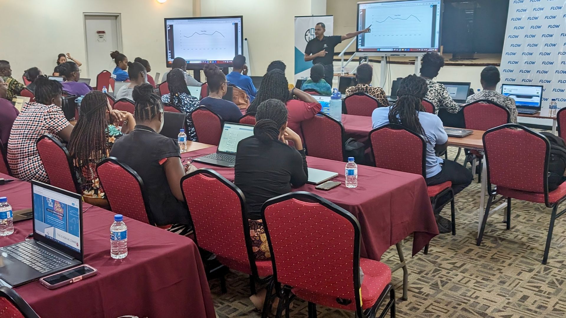 A group of people are sitting at tables in a room with laptops.