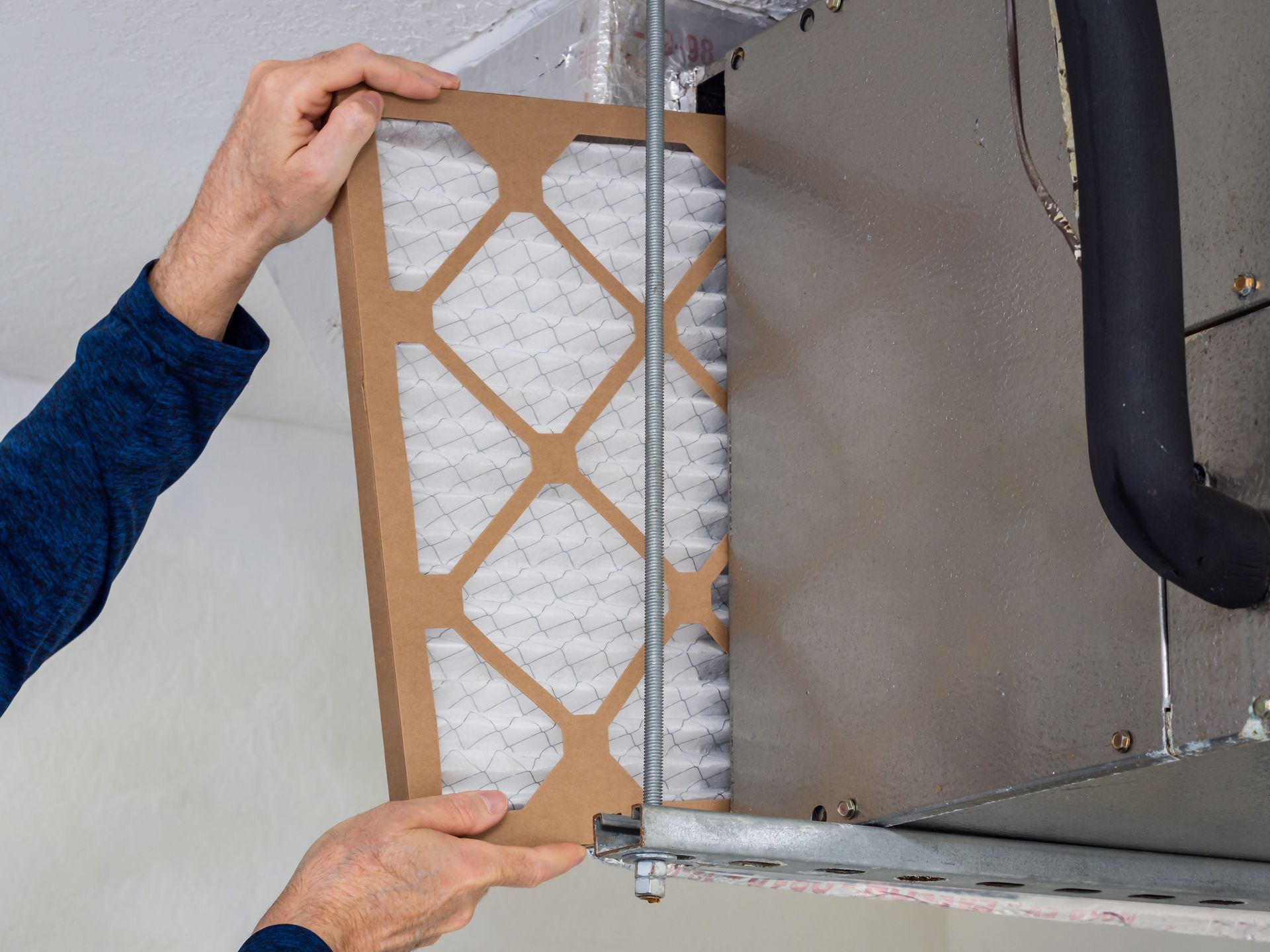 A person is holding a filter in their hands in front of an air conditioner.