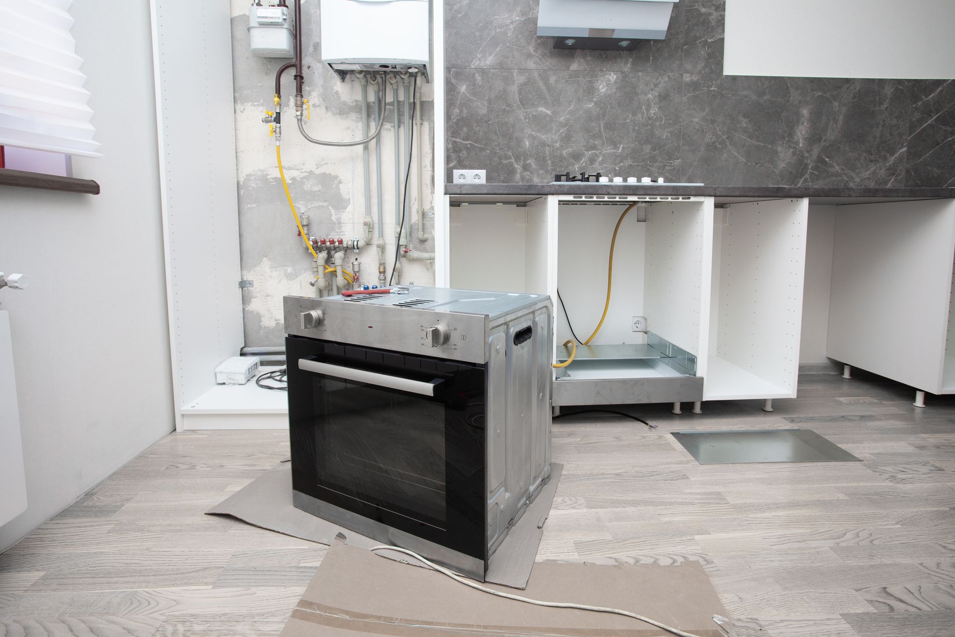 Oven on cardboard in front of kitchen cabinets and gas lines during renovation.