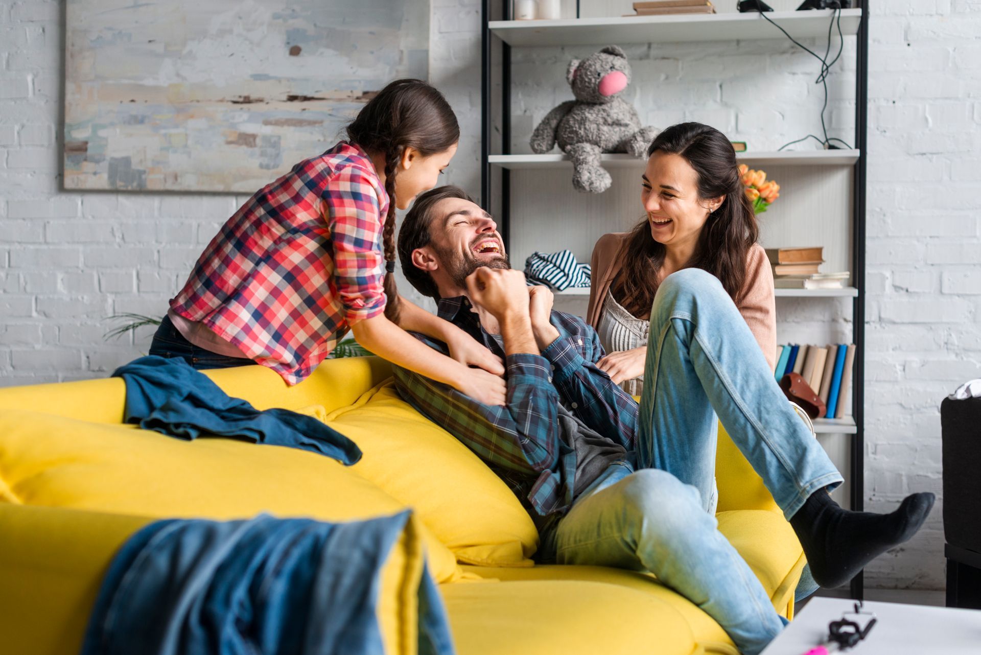 A family is playing on a yellow couch in a living room.