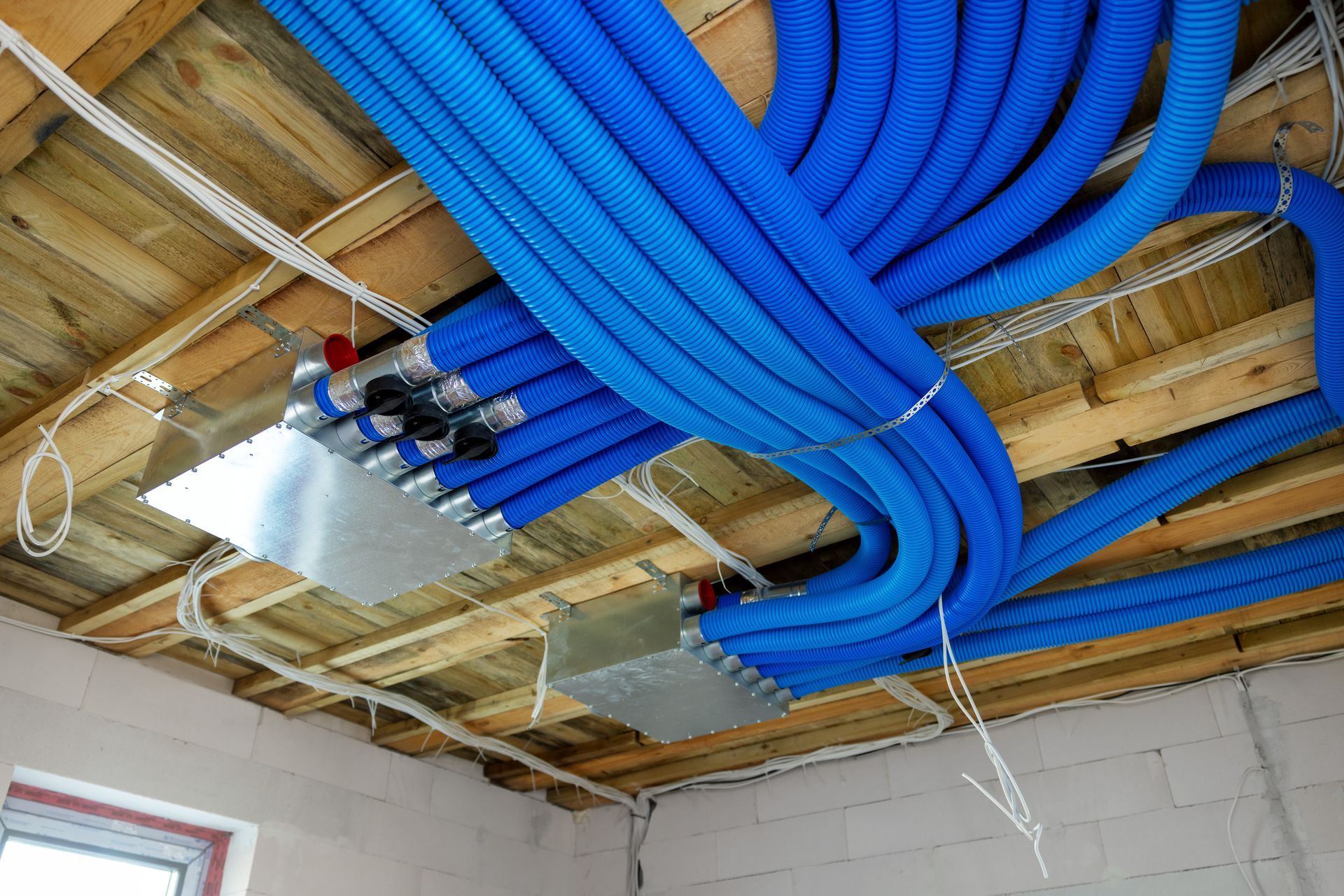 Blue flexible ductwork connected to a metal distribution box, mounted on a wooden ceiling.
