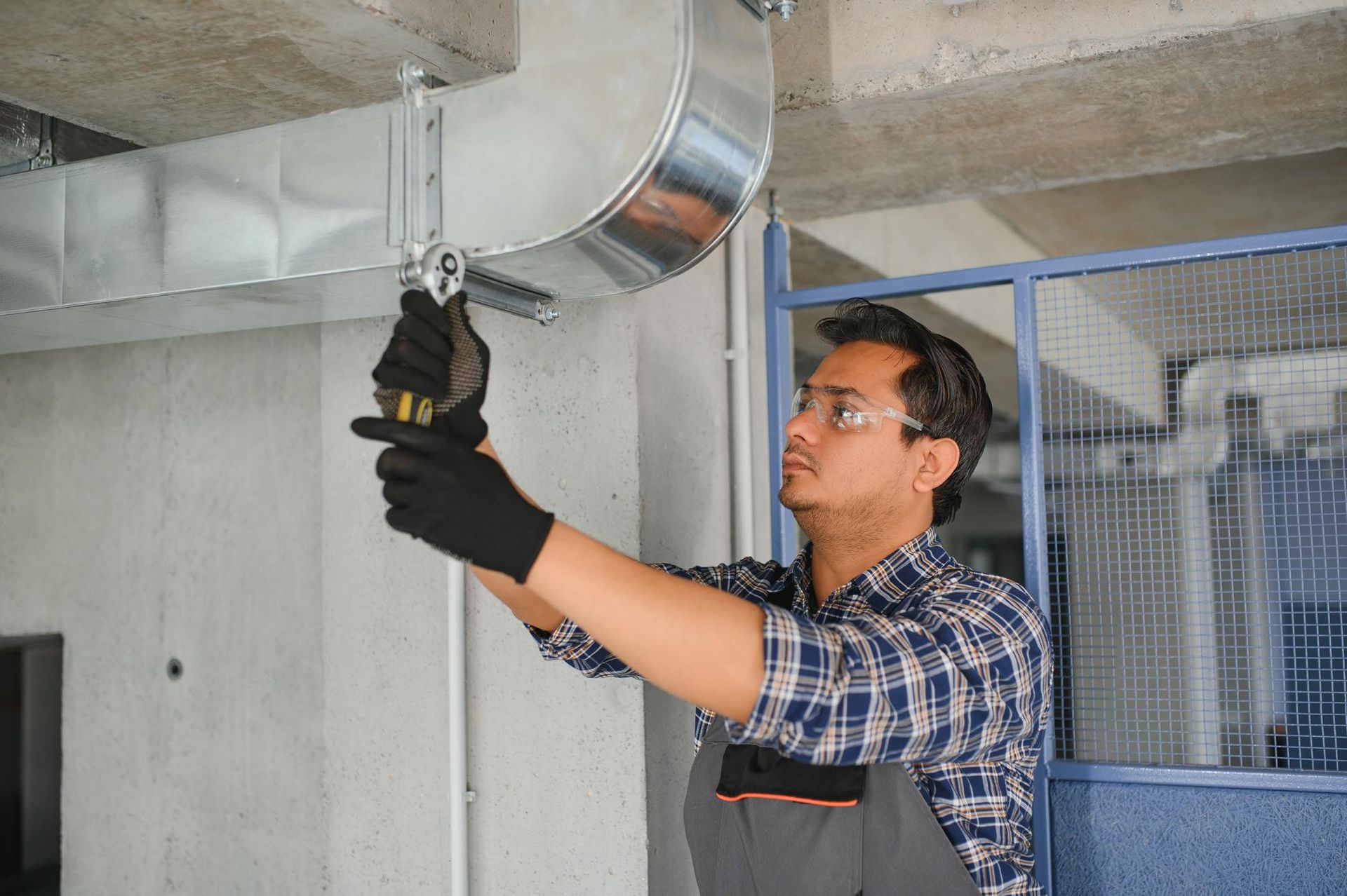 Man in safety glasses and gloves installing HVAC ductwork with a wrench.