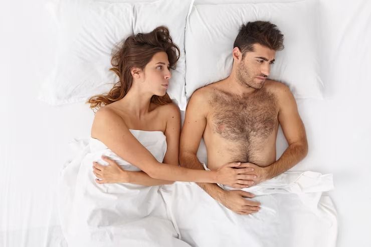 Un hombre y una mujer están acostados en una cama con sábanas blancas.