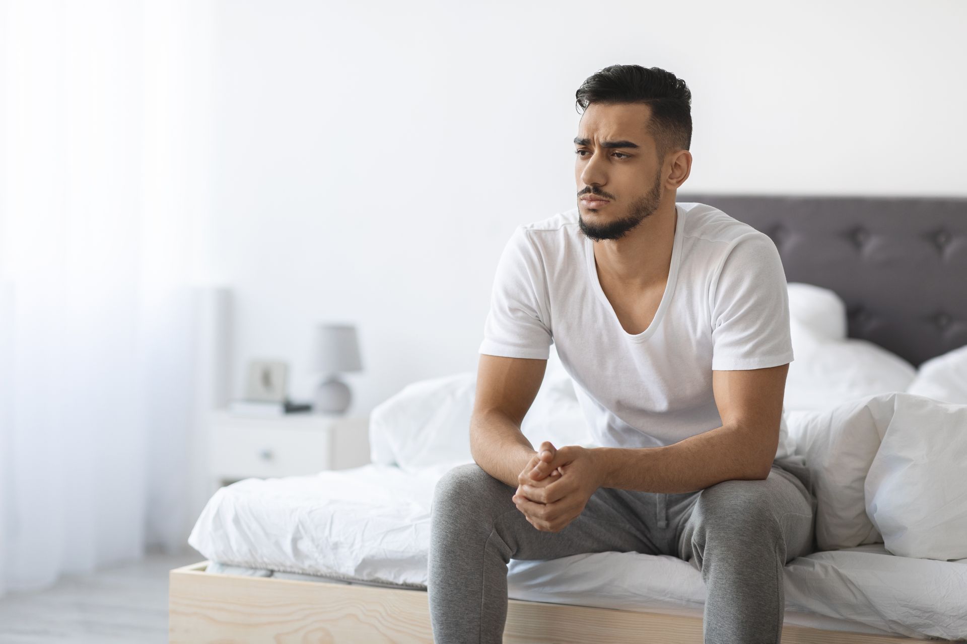 Un hombre está sentado en una cama mirando por la ventana.