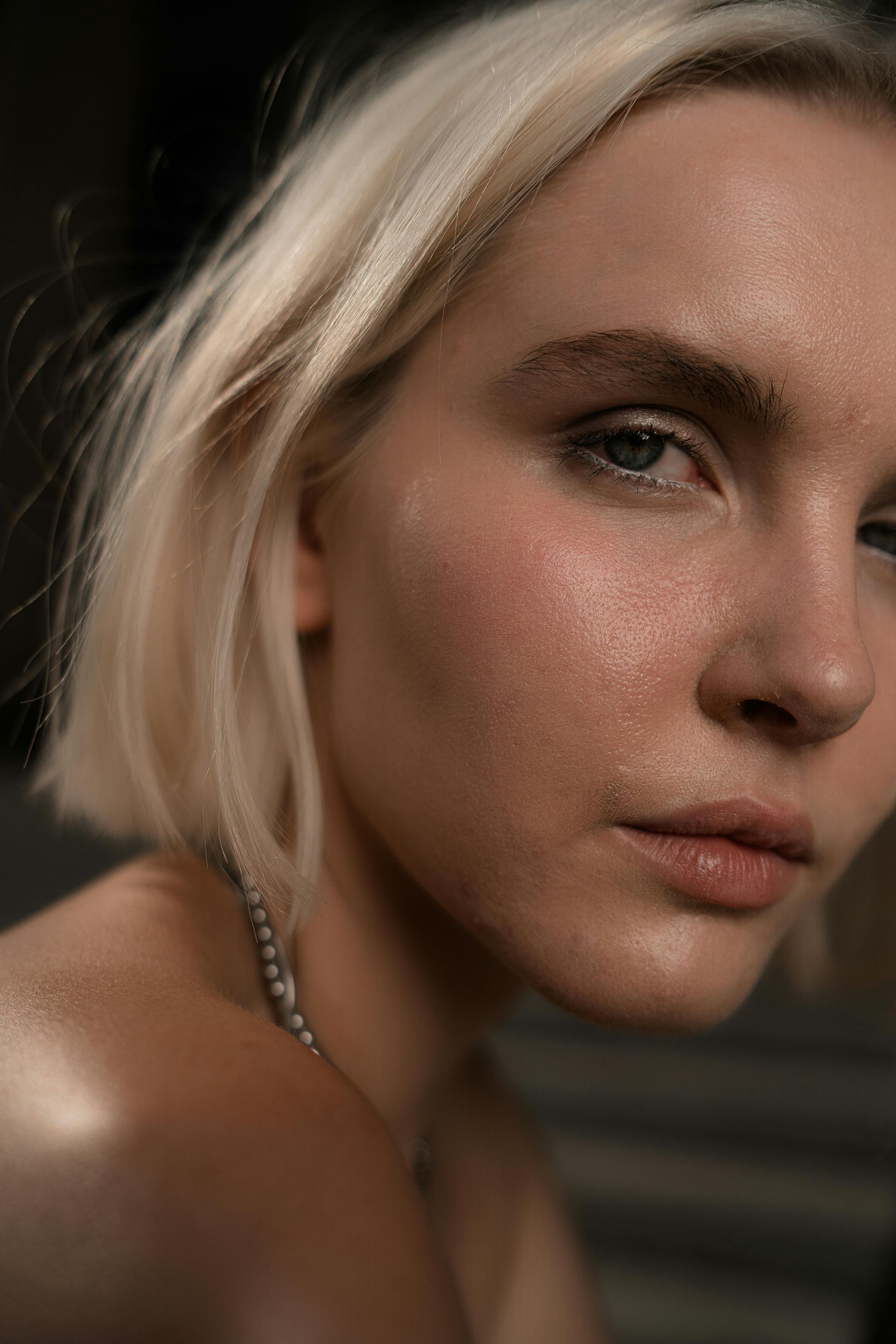 A close up of a woman 's face with short blonde hair and a necklace.
